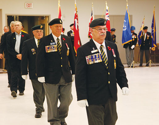 Le représentant national, Paul Poirier, devant l’ancien président de la Division du Manitoba-Nord-Ouest de l’Ontario, Rick Bennett (second à p. de la d.), et les autres invités se rendant sur l’estrade. [PHOTO : ADAM DAY]