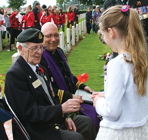 Une petite fille donne un coquelicot à Roy Eddy au cimetière militaire canadien de Bretteville-sur-Laize. [PHOTO : SHARON ADAMS]